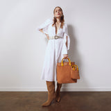 Model in a white dress and boots holding the Gisele Large Shopper in tan suede