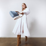Model in a white dress and boots holding the Lola Mini Shopper in blue suede