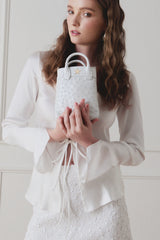 Model in a white outfit holding the Lola Mini Shopper in white ostrich