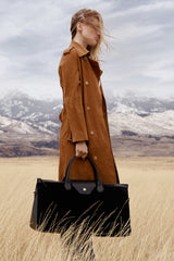 Model in a suede coat in a mountain meadow carrying the Maverick Weekender in black suede