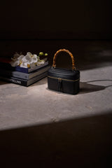 Mia Vanity Bag in black nappa leather resting on a table in a softly lit, dark interior