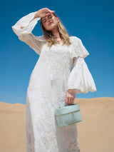Model in a white dress on sand dunes holding the Mia Vanity Bag in light blue ostrich