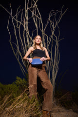 Model standing in front of bare branches at night with the Taylor Mini Clutch in blue ostrich