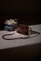 Taylor Mini Clutch in cheetah print calf hair resting on a table in a softly lit, dark interior