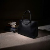 Alessia Large Tote in black nappa leather resting on a table in a softly lit, dark interior