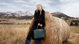 Model carrying the Alessia Large Tote in bottle green suede outdoors, with mountains in the background