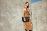 Model standing against a textured wall holding the Blake Large Clutch in black ostrich
