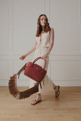 Model walking with a red handbag worn on the Fringe Shoulder Strap in chocolate nappa leather