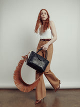 Model in tan trousers carrying a black handbag on the Fringe Shoulder Strap in tan nappa leather