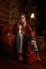Model seated in a leather armchair in a warmly lit room with the Lucille Mini Tote in begonia suede