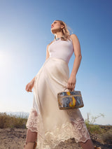 Model standing outdoors under a blue sky holding the Mia Vanity Bag in desert sky python
