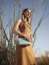Model standing among bare desert branches wearing the Taylor Mini Clutch in light blue ostrich crossbody